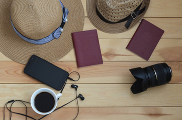 A cup of coffee, cell phone, straw hats, lens, and two passports on a wooden table. Space for text. Set for vacation.