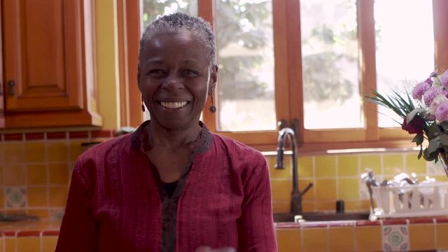 Older Senior Black Woman Dancing In A Kitchen And Looking At The Camera