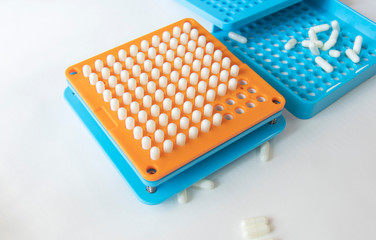 White pill capsules are row in orange filling machines hold by hand