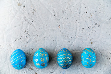 Eggs painted in blue and with a gold pattern on a concrete background.