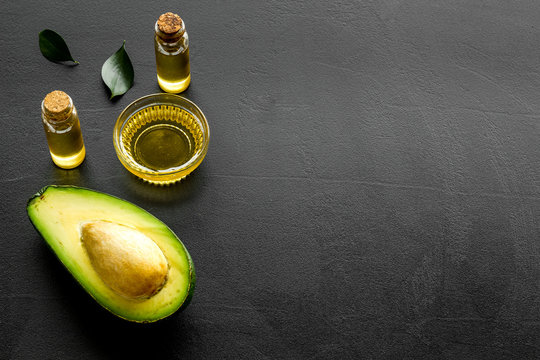 Avocado oil for cosmetology. Sltill lfe with half of fruit and bottles on black background copy space