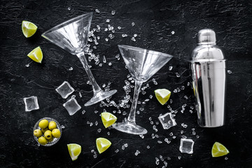 Bar background with martini glasses, shaker, ice, lemon and olives on black table top-down