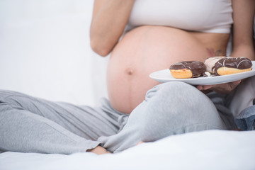 beautiful young pregnant woman holding sweet donut in her hand. expectation of the child, pregnancy and motherhood. healthy and unhealthy eating concept, diet. Junk food. soft focus background