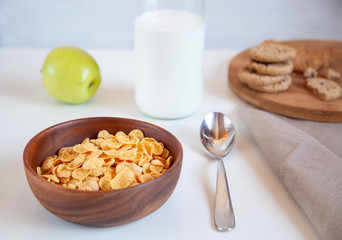 Corn flakes in a wooden plate and bottle of milk on the table.