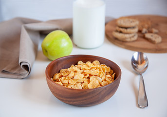 Corn flakes in a wooden plate and bottle of milk on the table.