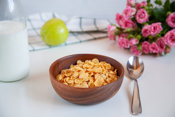 Corn flakes in a wooden plate and bottle of milk on the table.