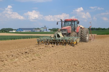 Fototapeta premium Semis mais avec semoir 32 rangs de 4m et outil ottavioli (tasseligne) à l'avant. Coopérative agricole en arrière plan