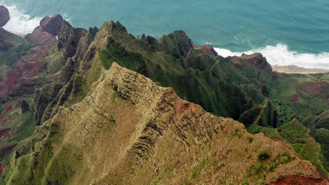 Inspiring aerial 4K view over the exotic island coastline formed by high winding ridges and deep narrow gorges. Sun enlights the tops of the rocks. Vibrant blue ocean looks smooth and calm. Hawaii,USA