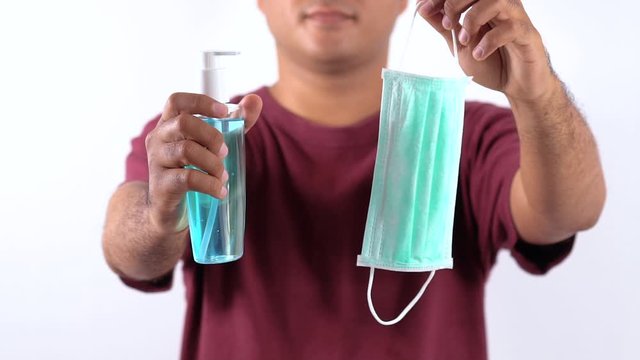 Close-up hand holding plastic bottle pump with alcohol hand gel and protection mask. Coronavirus or covid 19 concept.