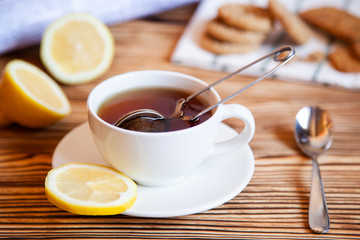 Cap of tea with lemon and cookies on the wooden table.