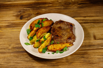 Fried beef steak with potato wedges on wooden table