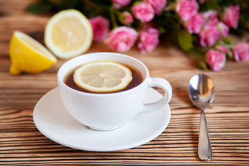 Obraz na płótnie Canvas Cap of tea with lemon and flowers on the wooden table.