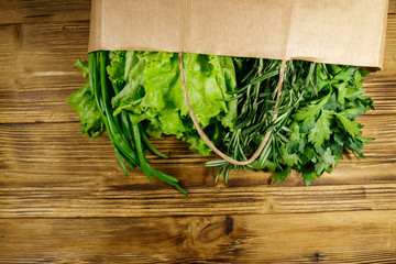 Paper bag with green onion, rosemary, lettuce leaves and parsley on wooden table. Top view. Healthy food and grocery shopping concept