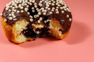 Bitten tasty chocolate donut on a pink background