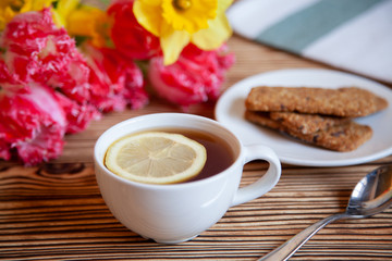 Cap of tea with lemon and flowers and cookies on the wooden table.