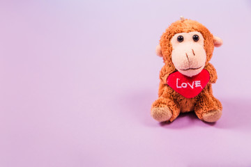 Soft toy monkey holding a heart in his hands on a purple background