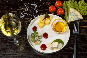  Assorted cheeses with honey and green leaves on a plate. Appetizer for white wine.