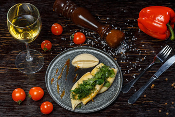 Dish from a chef of sea fish with parsley and dill. White wine in a glass, tomatoes, bell pepper and seasonings.