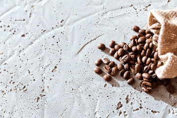 Coffee beans falling out burlap sack isolated in cement background, Top view with copy space for your text message or promotional content.