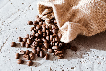 Coffee beans falling out burlap sack isolated in cement background, Top view with copy space for your text message or promotional content.