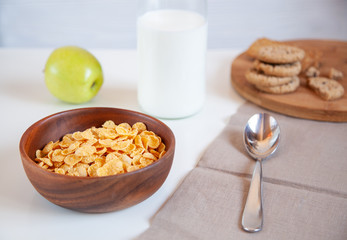 Corn flakes in a wooden plate and bottle of milk and apple on the table.