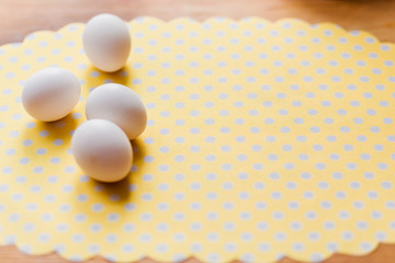 White chicken eggs on a wooden table on a yellow polka dot napkin