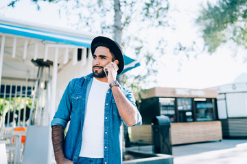 Joyful adult ethnic man talking on phone on street in daytime