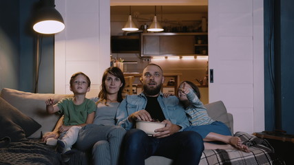 Happy positive young Caucasian family with children watch movies expressing different emotion at home on couch together.
