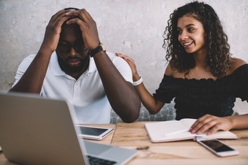 Curly woman cheering sad African American coworker