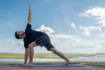 Man wearing a black shirt and dark green shorts bends over in a triangle pose correcting his bodies...