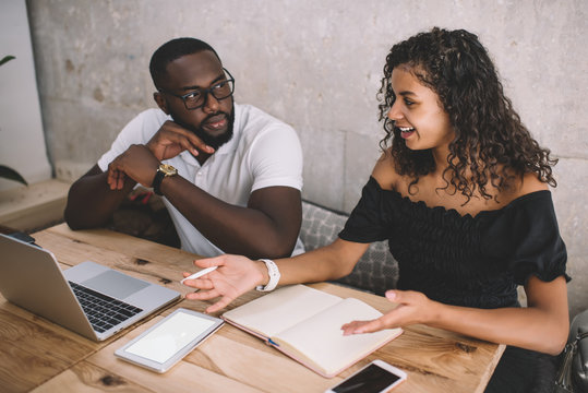 Multiracial couple communicating at table using laptop and devices