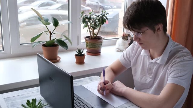 Young man studying at home using laptop. Home school, online education, home education, quarantine concept. 4k footage.