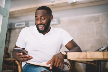 Cheerful surprises dark skinned male millennial checking notification about winning opportunity in online contest, happy 20s african american hipster guy getting discount for web store on smartphone