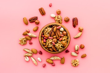 Mixed nuts in bowl on pink background top-down frame