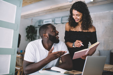 Prosperous dark skinned male and female colleagues discussing collaboration planning checking notes...