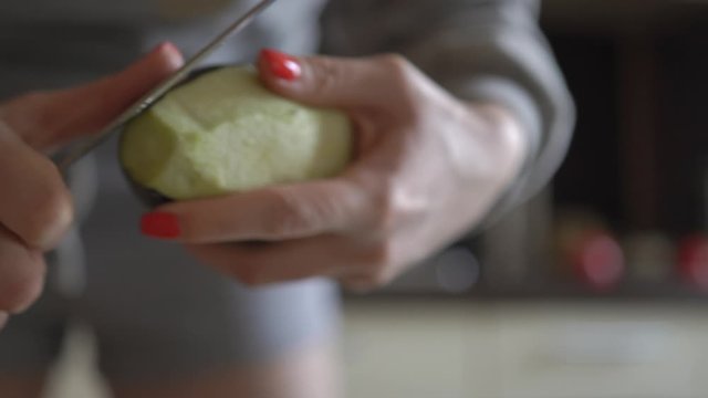 Girl in home clothes kitchen preparing food. Cleans eggplant peel large uncomfortable blunt knife which spoils pleasure cooking Tears off pieces cleans unevenly Advertising cleaners kitchen appliances