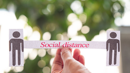 ็ืHand holding text "Social distance" and paper man model green  background, have copy space. Concept  Social distance to stop the outbreak covid-19