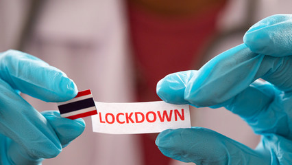 The doctor wears blue gloves holding note paper have text  "Lockdown"  and  Thailand flag.   Concept Lockdown covid-19.