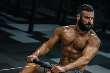 Fototapeta na wymiar Muscular fit man having functional training with rowing machine in gym