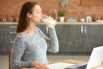 Beautiful young woman with laptop drinking milk at home