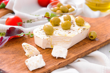 Board with tasty feta cheese, olives and spices on table