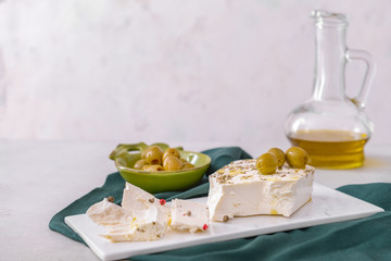 Tasty feta cheese with olives, spices and oil on white background