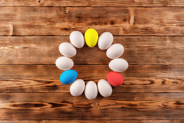 Ring or circle of chicken eggs painted in different colors and white on a wooden background top view. Copy space.