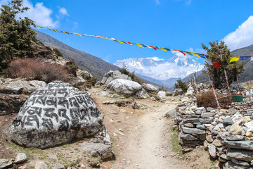 Everest and Lhotse mountain peaks rises above footpath leading to Everest base camp. Prayer flags...