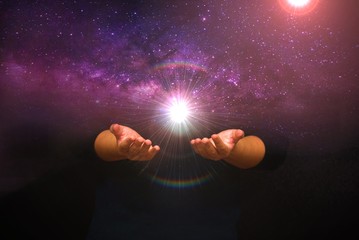 Spiritual image: hands with shining light ball on universe background, spiritual power concept.