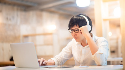 Young Asian man wearing headphones listening to music while working with laptop computer. Male office worker doing online conference with his business company team. Work from home concept