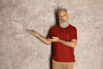 Obraz na płótnie Canvas Presenting your product. Confident senior man in casual wear pointing away and looking at camera while standing against grey background.
