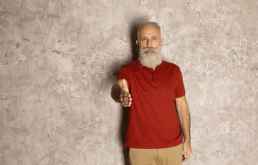 Naklejka na ściany i meble Elderly gray-haired mustache bearded man in T-shirt posing isolated on grey background. People lifestyle concept. Standing with outstretched hand for greeting.