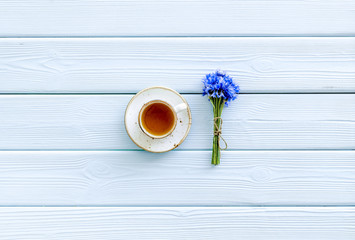 Fototapeta na wymiar Summer tea party. Cup near cornflowers bouquet on blue wooden background top-down copy space