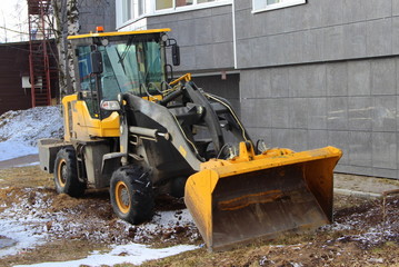 A black and yellow wheeled tractor stands against a wall of a house. Heavy construction machinery concept